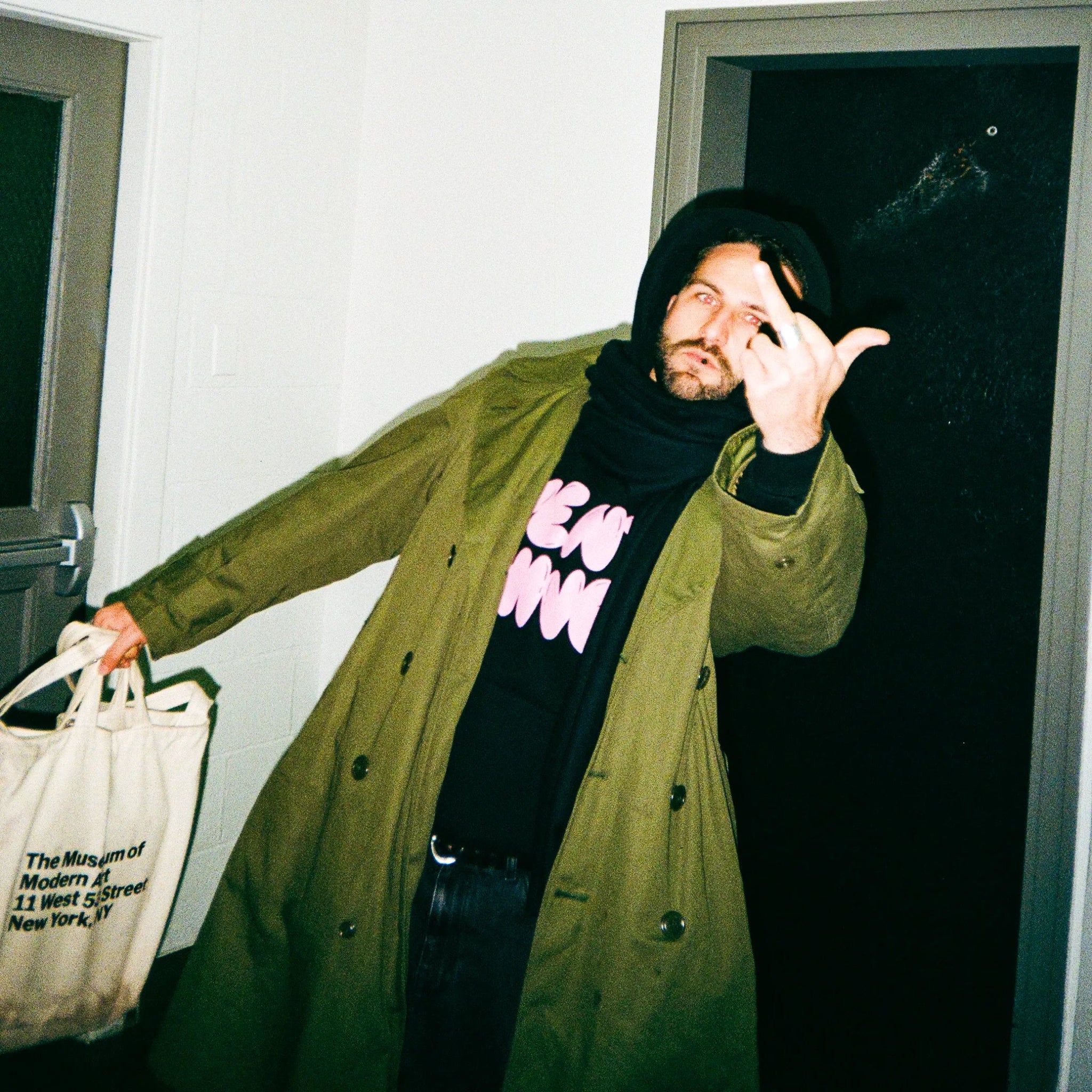 Person wearing a green coat and black hoodie with pink text by VENT D'HIVER, holding a white bag.